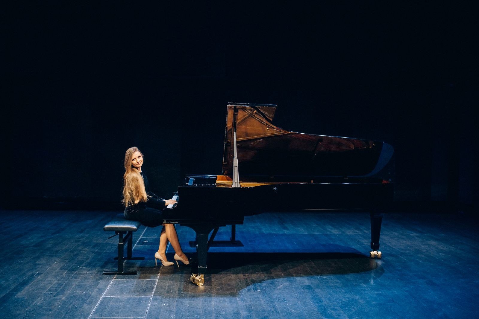 Pianista sentada ao piano de cauda em um palco escuro iluminado de azul, imagem ilustrativa