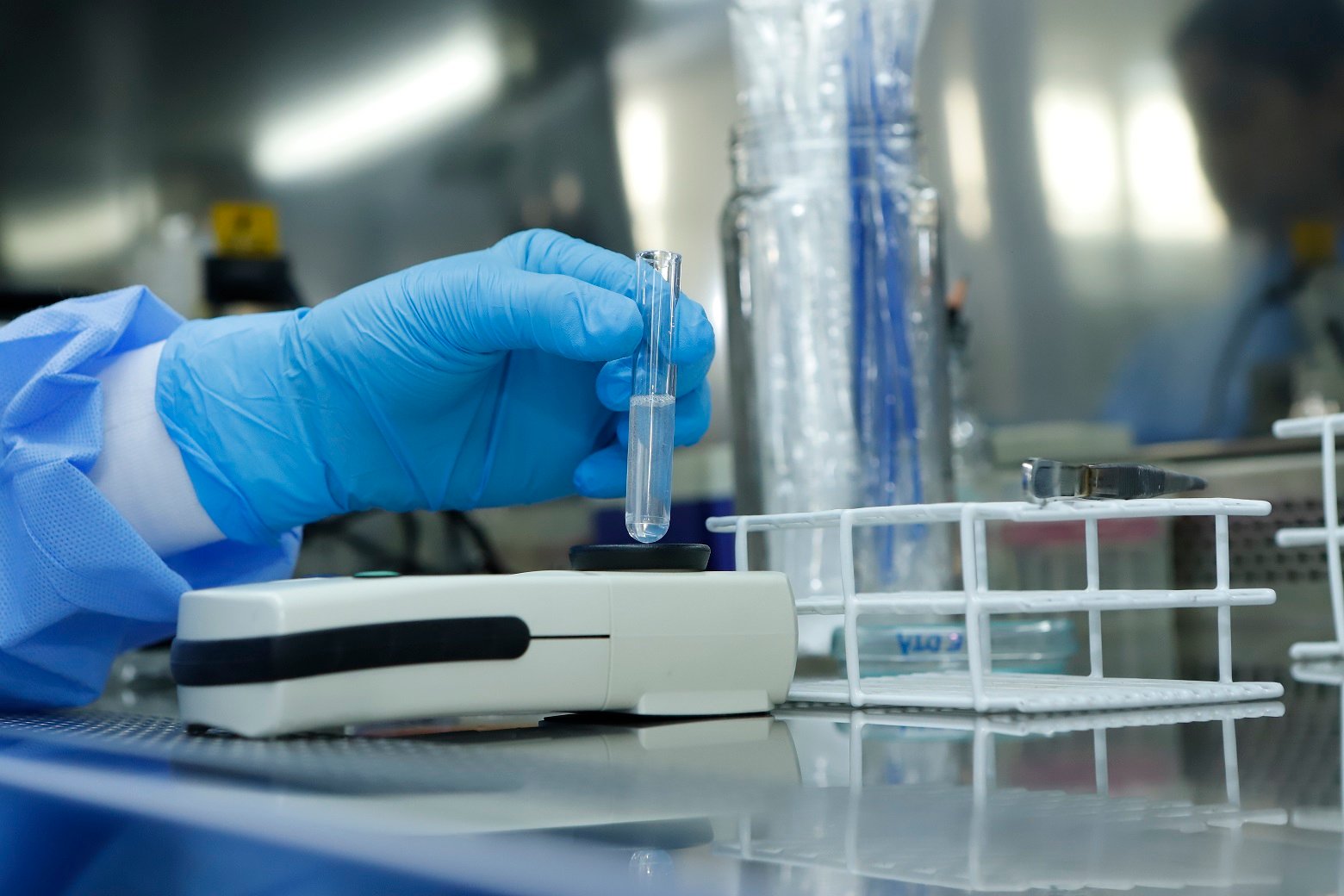 Profissional de laboratório com luvas azuis manipula tubo de ensaio com amostra