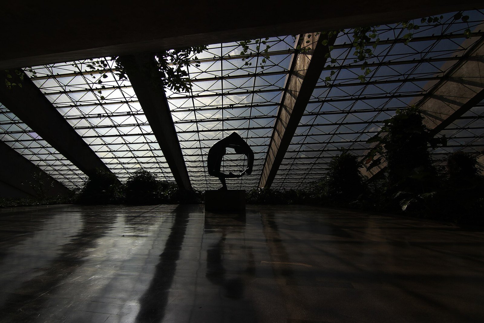 Foyer do Teatro Nacional em contraluz, com escultura sobre pedestal diante da parede de vidro estruturada