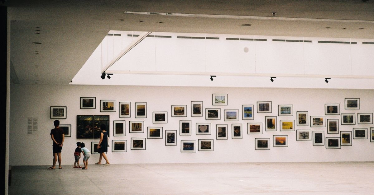Visitantes observam parede com dezenas de quadros emoldurados em galeria de arte
