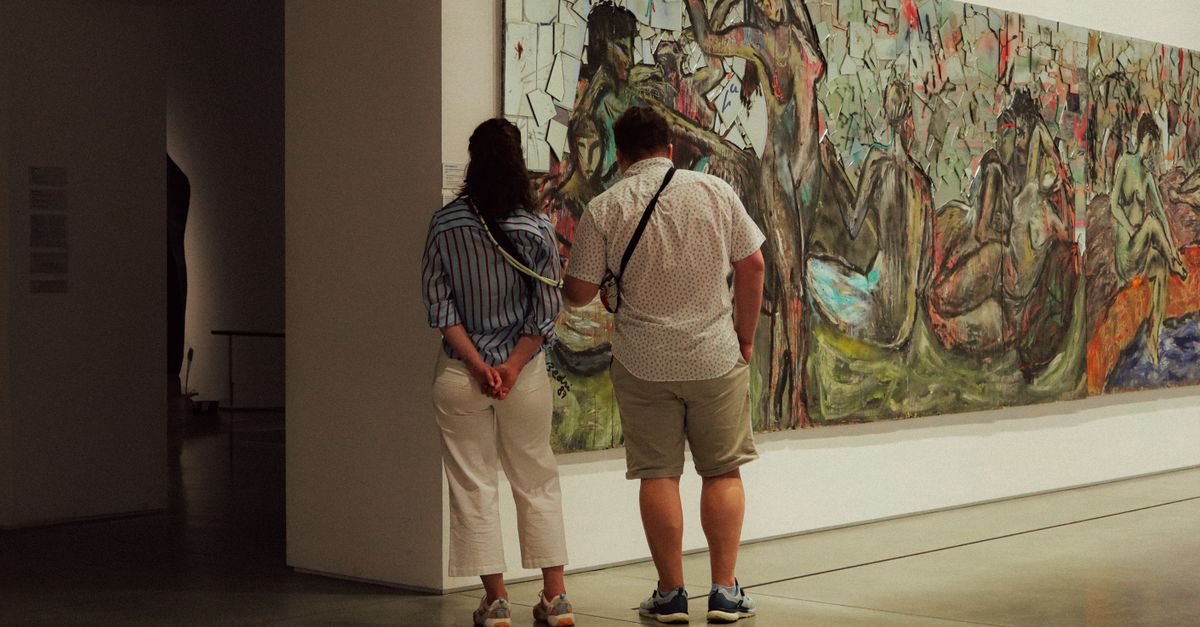 Duas pessoas observam uma pintura de grandes dimensões em sala de exposição