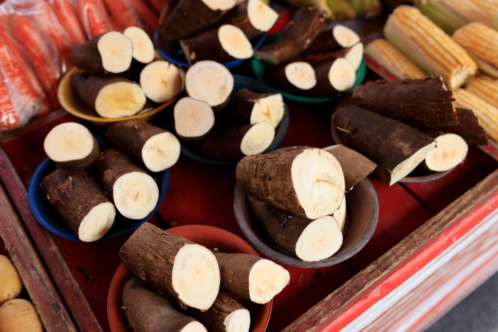 Pedaços de mandioca em bacias e espigas de milho numa banca de feira, foto ilustrativa