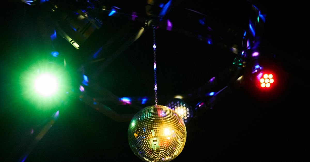 Globo de espelhos dourado suspenso em pista de dança iluminada por refletores verde e vermelho