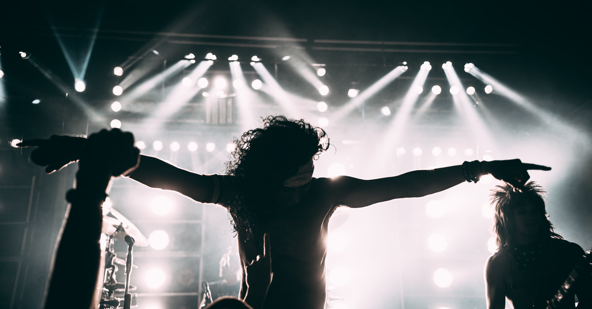 Vocalista de cabelo cacheado abre os braços diante de refletores em show de rock