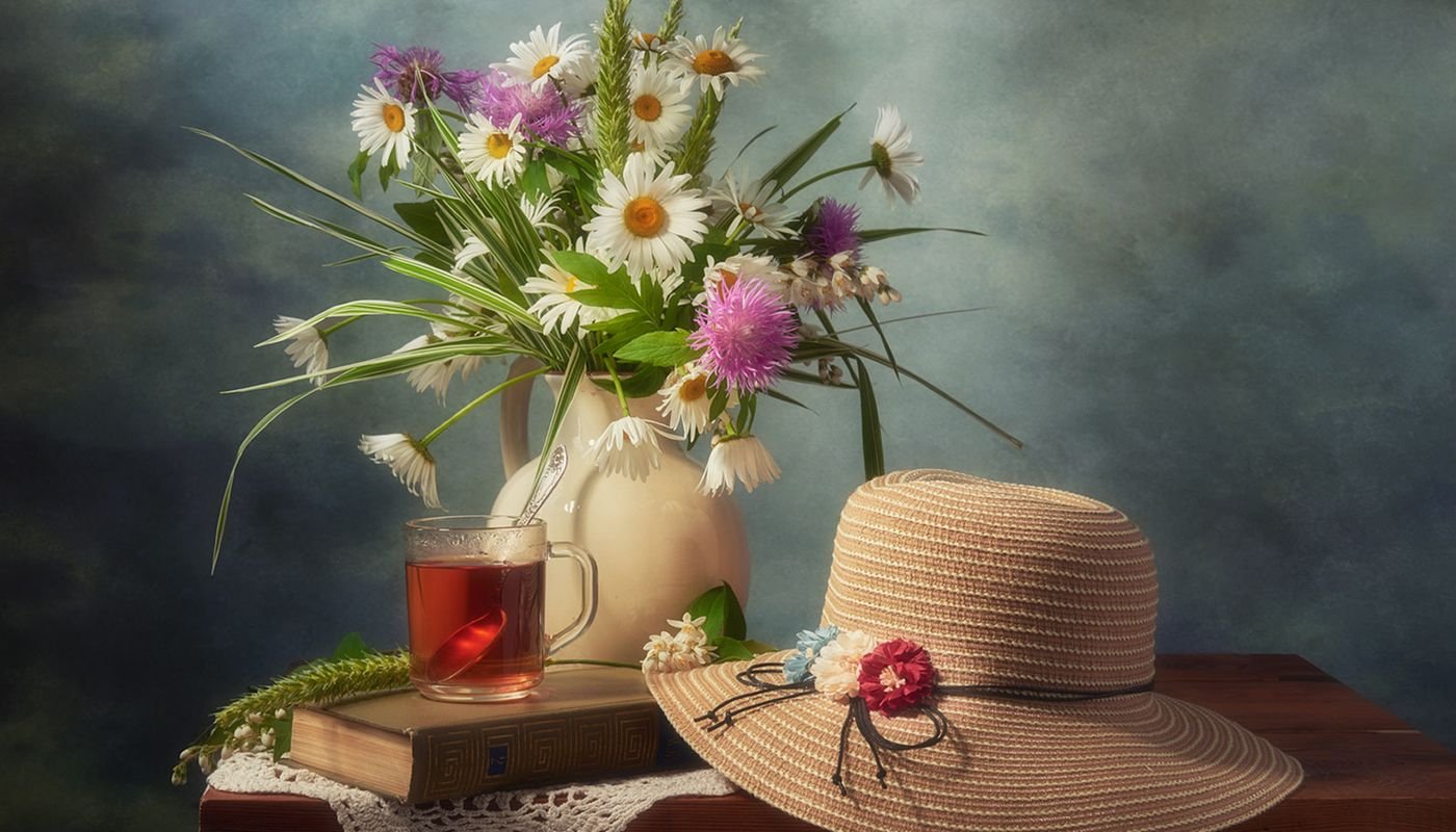 Chapéu feminino de palha com flores ao lado de buquê e xícara de chá na mesa