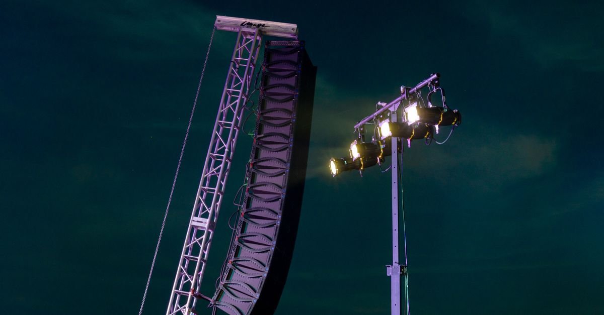 Caixas de som line array e refletores de palco montados em treliça contra o céu escuro durante show noturno