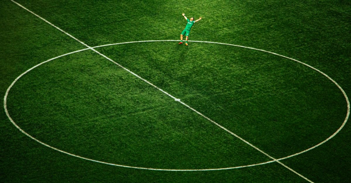 Jogador de futebol comemora sozinho no círculo central de um campo