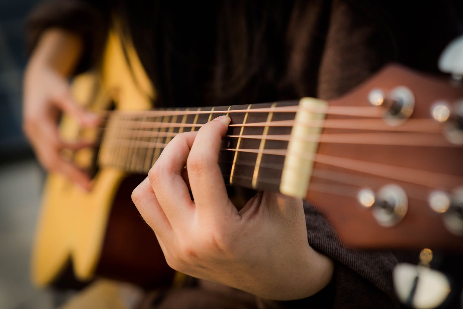 Mão pressionando as cordas de um violão acústico, em close