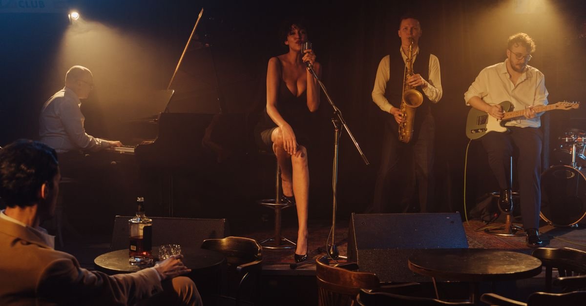 Banda de jazz toca em clube intimista com cantora ao microfone, piano, saxofone e guitarra