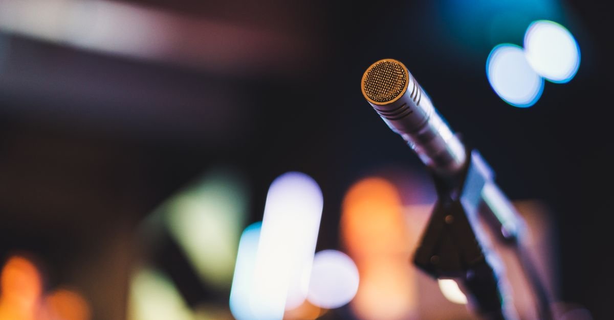 Microfone em pedestal sobre palco iluminado, com luzes desfocadas ao fundo