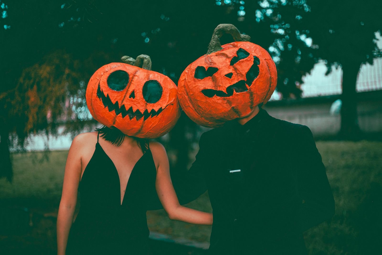 Casal com máscaras de abóbora de Halloween, uma de cada lado, em fundo de árvores
