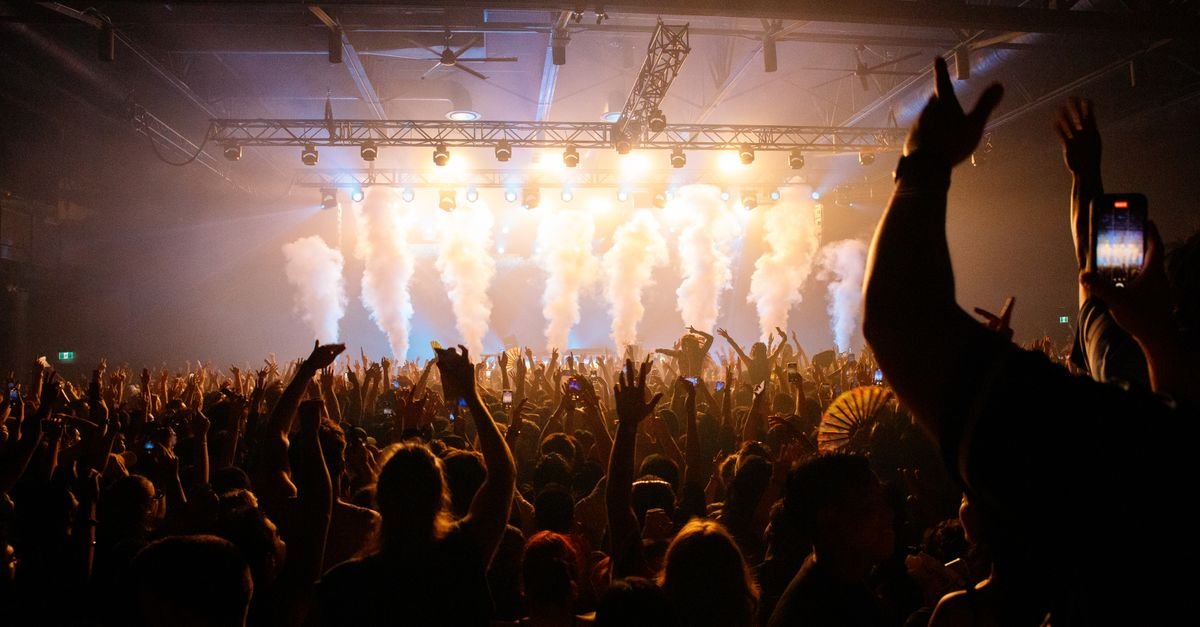 Público de braços erguidos diante de palco iluminado durante show