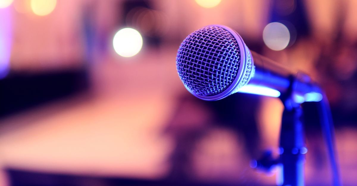 Microfone em pedestal iluminado por luzes de palco em tons de azul e roxo