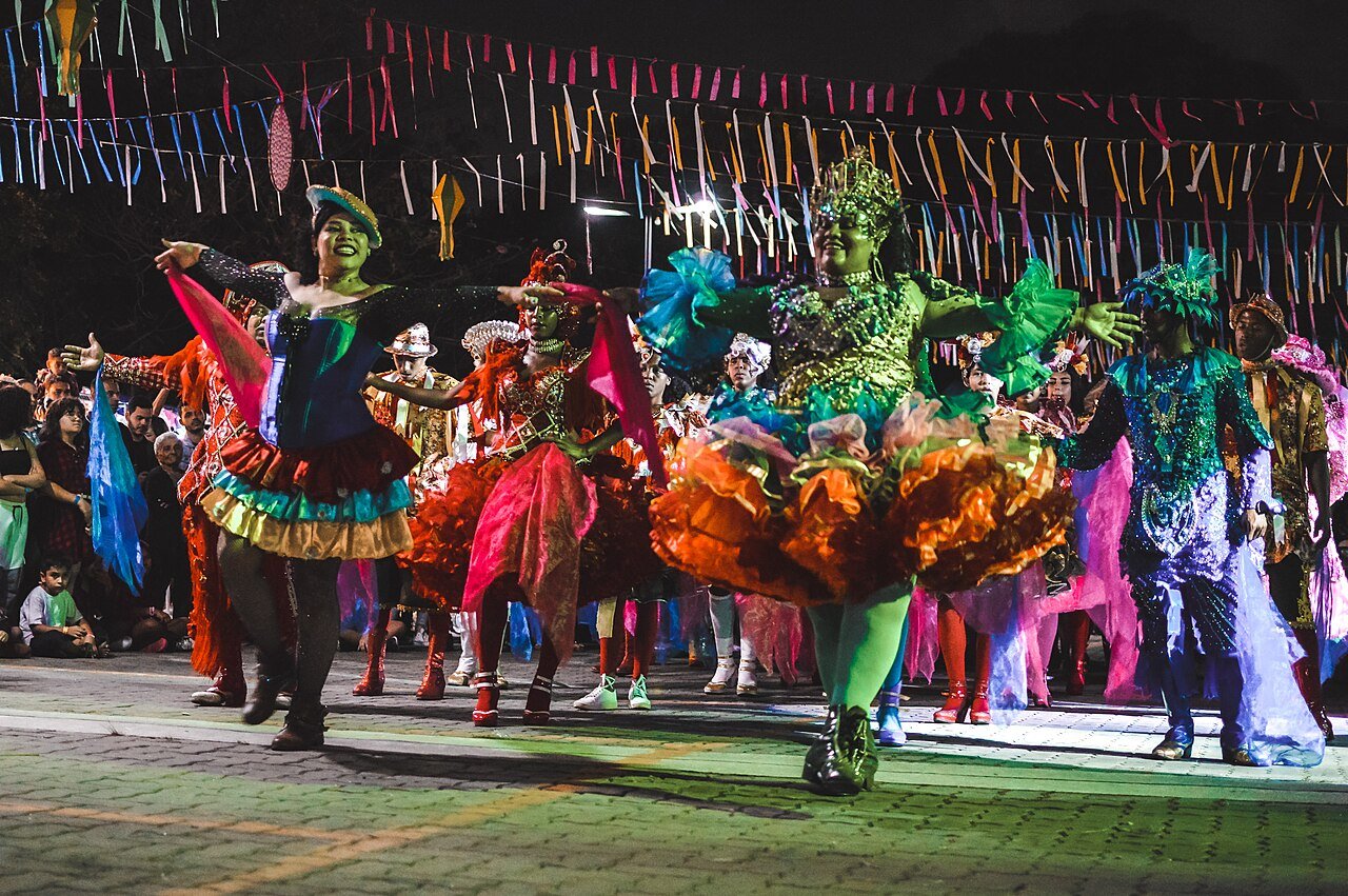 Dançarinos de quadrilha junina com trajes coloridos sob bandeirinhas durante apresentação
