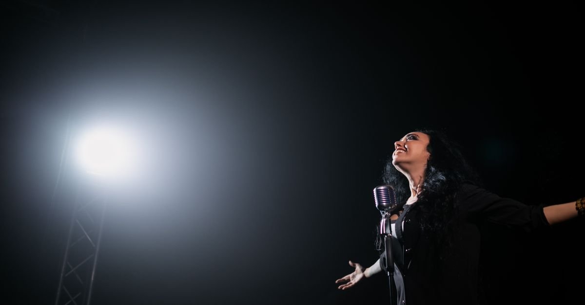 Cantora se apresenta em palco iluminado por refletor, imagem ilustrativa