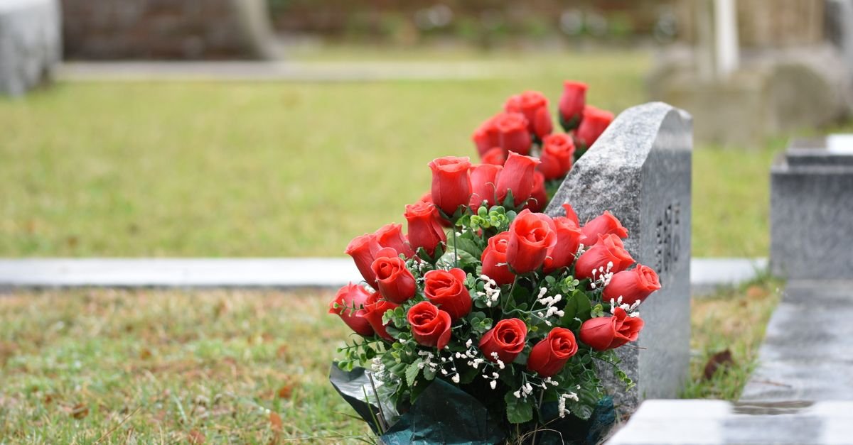 Buquê de rosas vermelhas apoiado em uma lápide de granito em cemitério