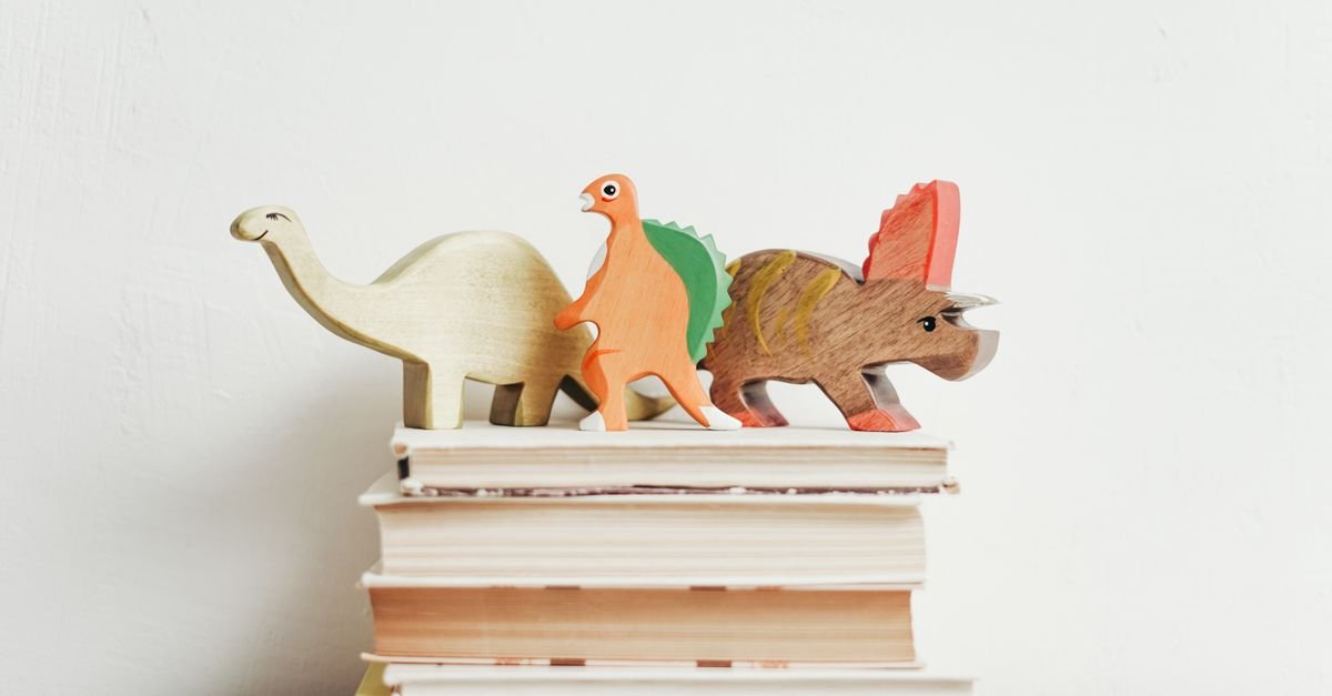 Dinossauros de madeira coloridos sobre uma pilha de livros infantis