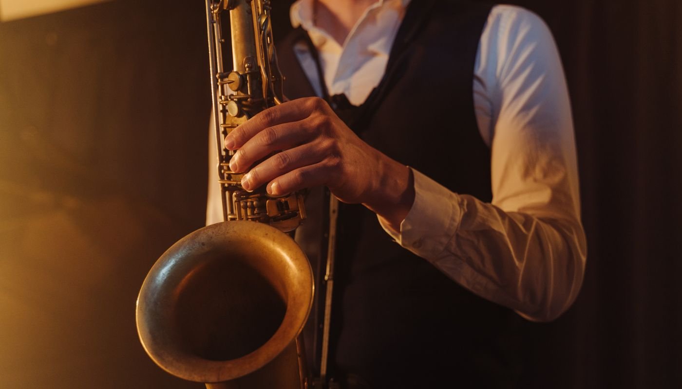Músico toca saxofone em ambiente com iluminação quente, em plano aproximado