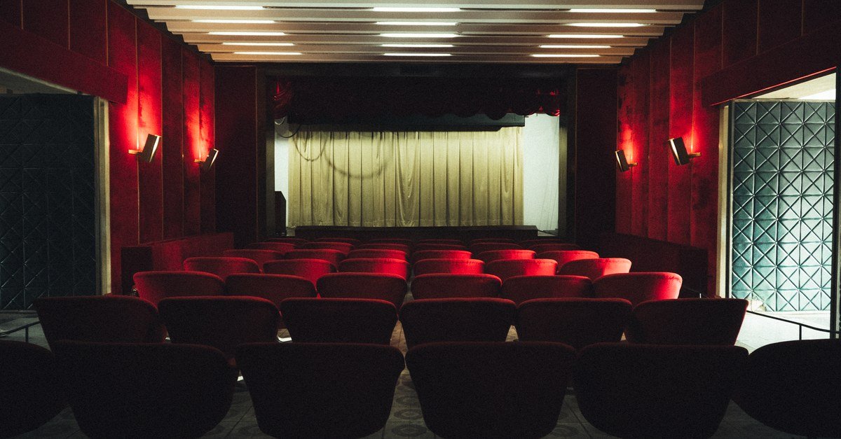 Plateia vazia de teatro com poltronas vermelhas e cortina de palco fechada antes do espetáculo