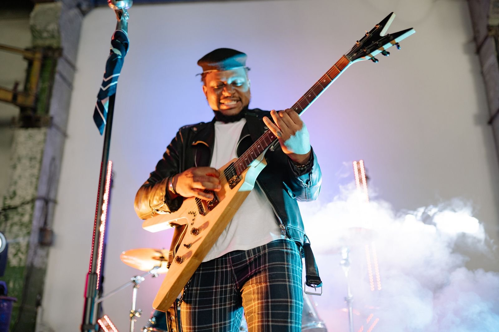 Guitarrista de jaqueta de couro toca guitarra em formato de V em palco com fumaça; foto ilustrativa de show de metal