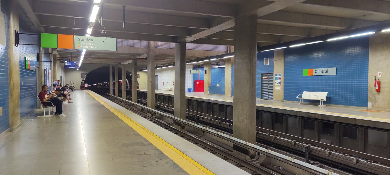 Plataforma da estação Central do Metrô-DF, com passageiros sentados e trilhos em primeiro plano