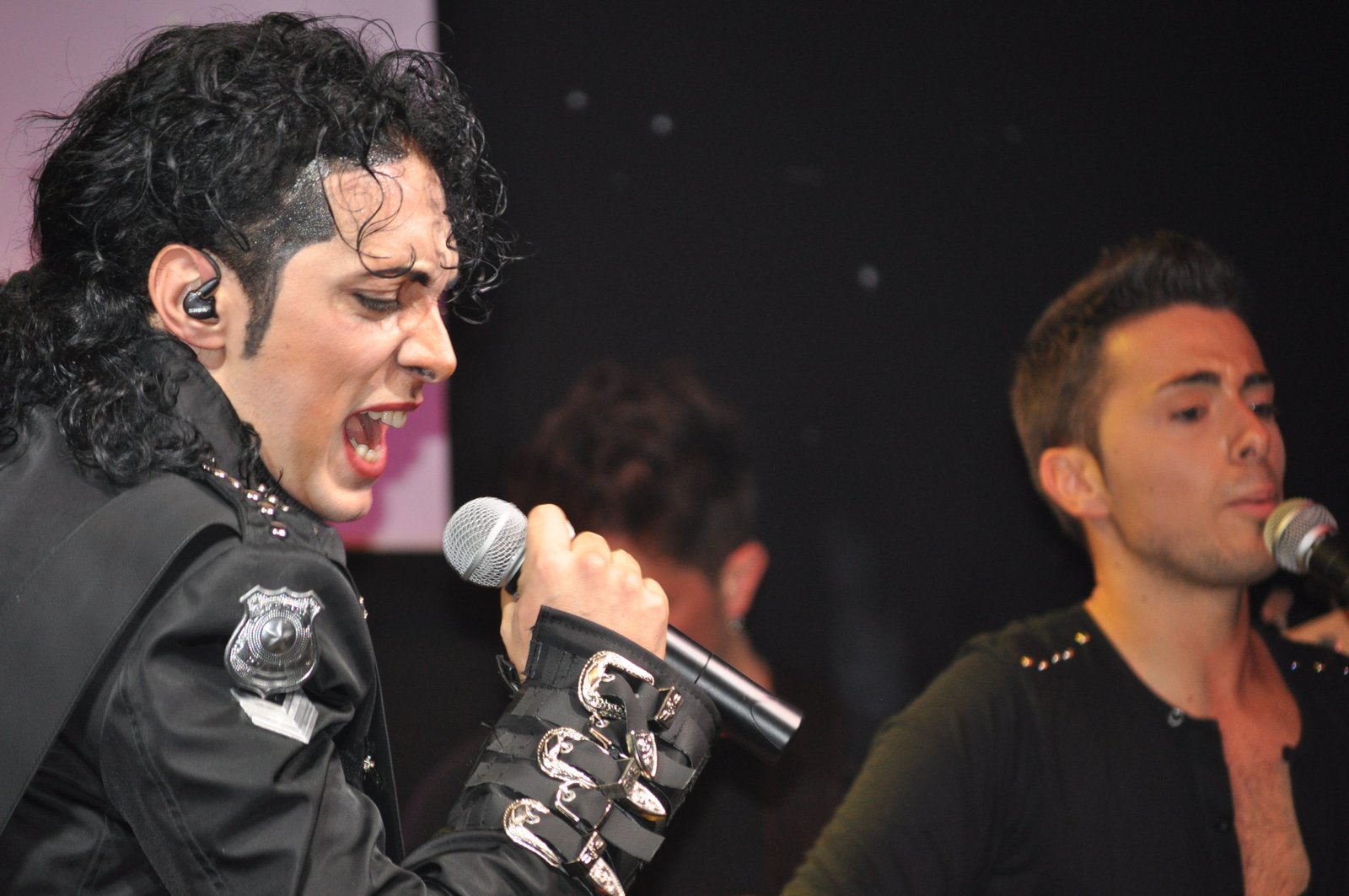 Artista com figurino preto e fivelas prateadas canta em show tributo a Michael Jackson
