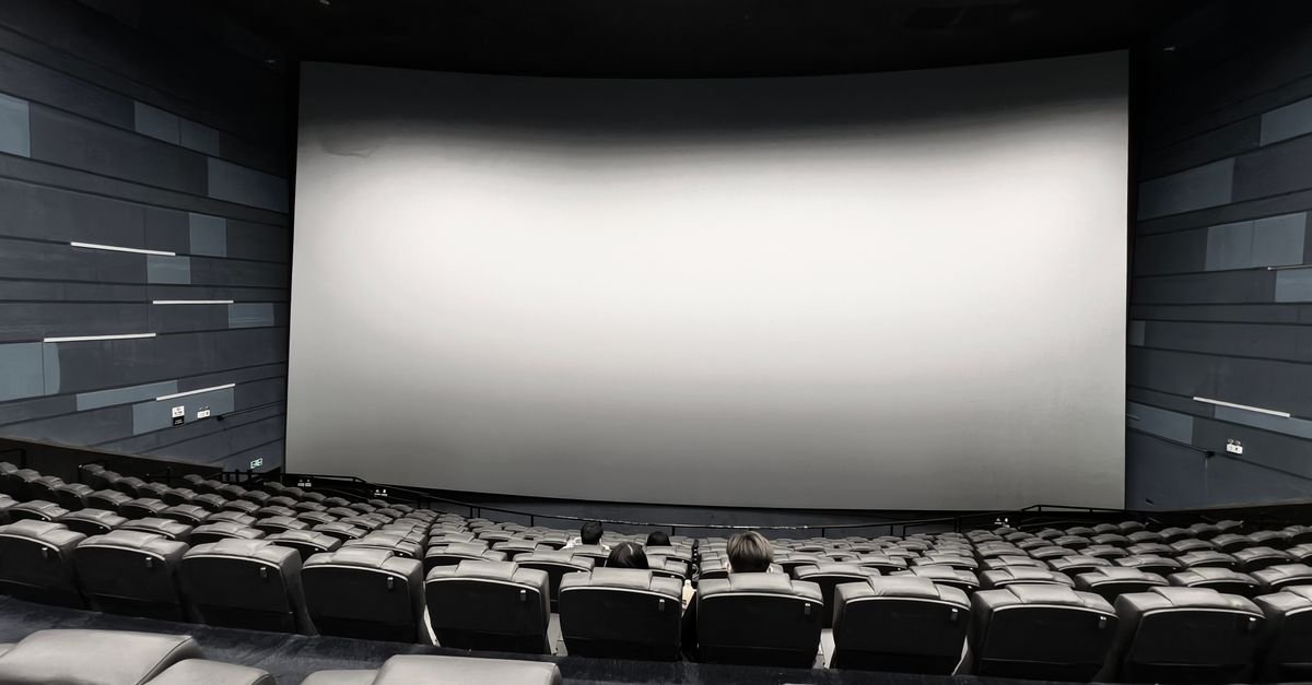 Sala de cinema com poltronas escuras e tela grande iluminada antes da sessão