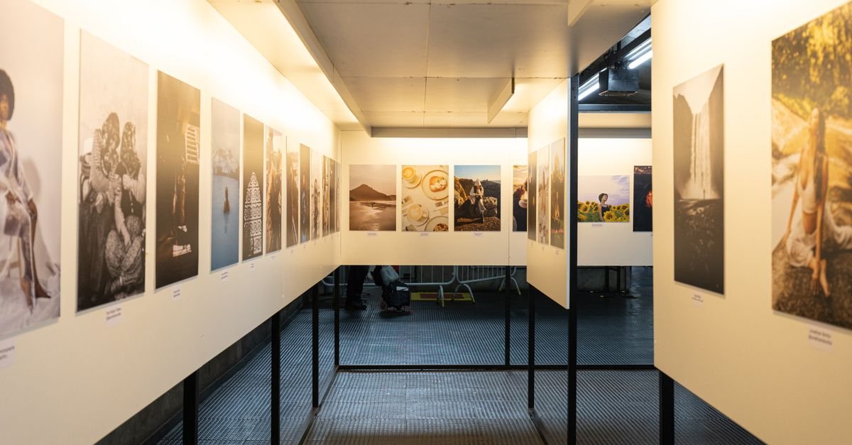 Corredor de galeria com fotografias emolduradas expostas em painéis iluminados