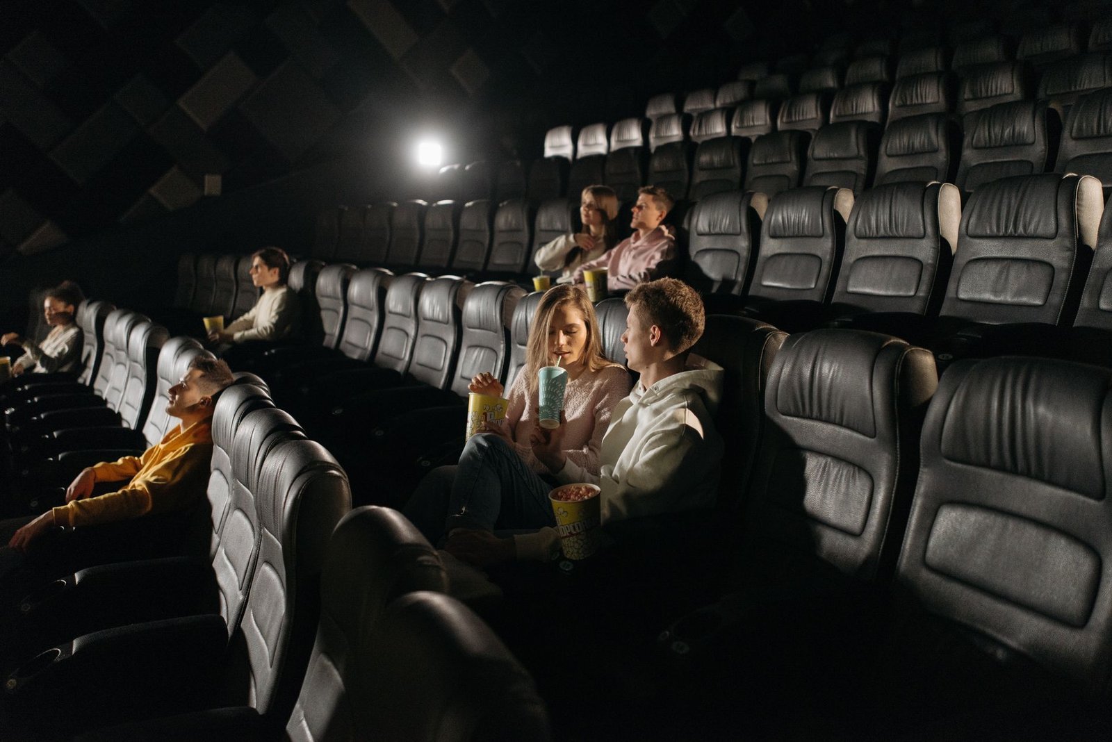 Espectadores em sala de cinema escura, com fileiras de poltronas pretas e pipoca