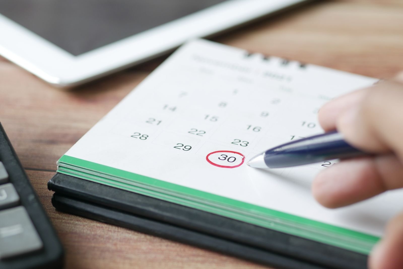 Mão com caneta marca o dia 30 em um calendário de mesa