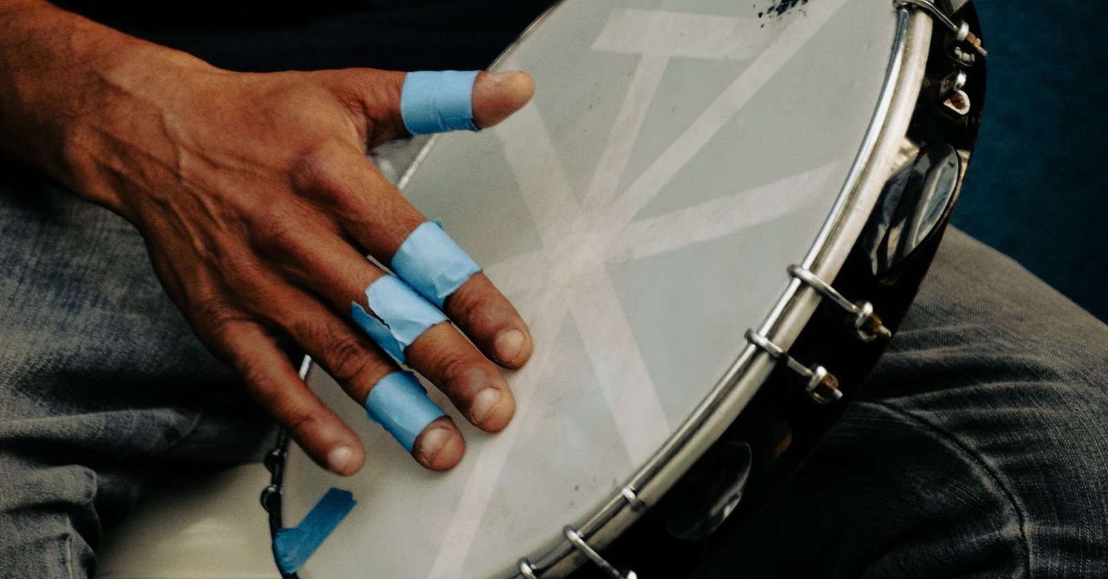 Mão com os dedos protegidos por fita azul tocando um pandeiro. Foto de banco de imagens, não é do bar.