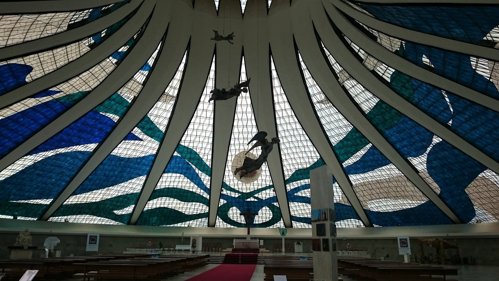 Interior da Catedral de Brasília visto do fundo, com os vitrais azuis e verdes de Marianne Peretti e os anjos de Alfredo Ceschiatti suspensos