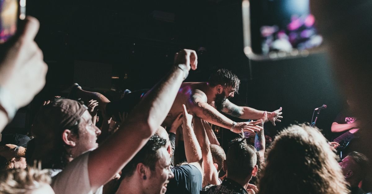 Músico é carregado pela plateia em show de rock sob luzes do palco