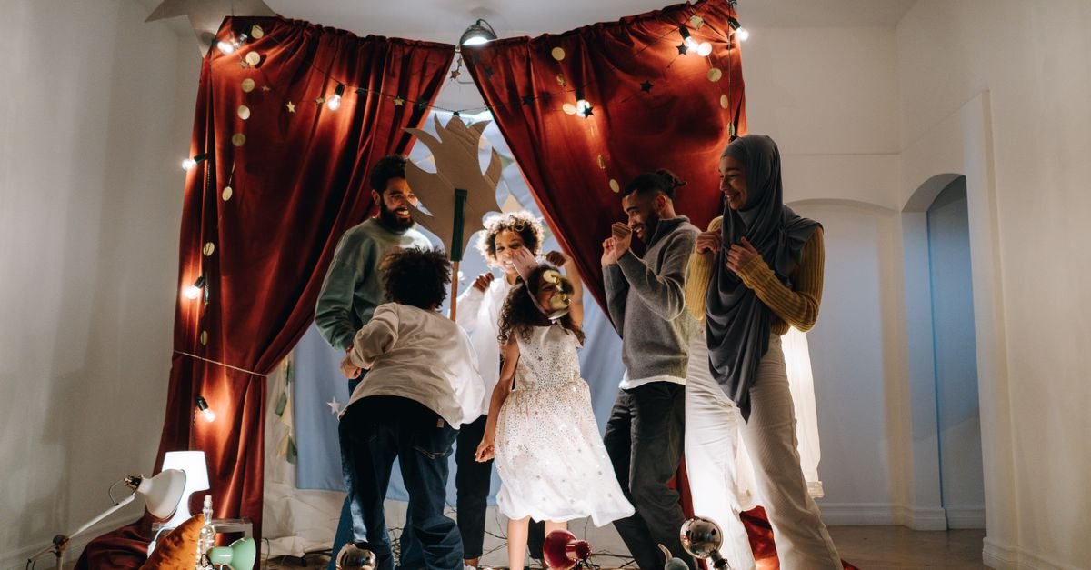 Família encena peça com criança em pequeno palco com cortinas vermelhas e luzes