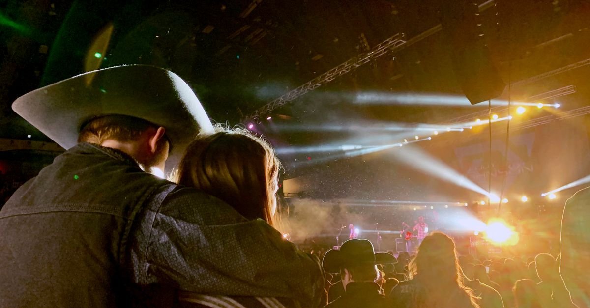 Casal de costas, homem de chapéu de caubói, assiste a show com luzes no palco