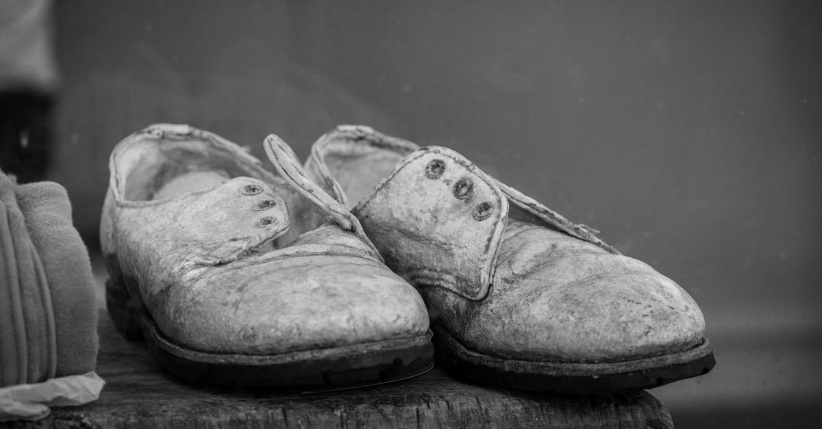 Par de sapatos de couro antigos e desgastados sobre superfície de madeira, em fotografia preto e branco