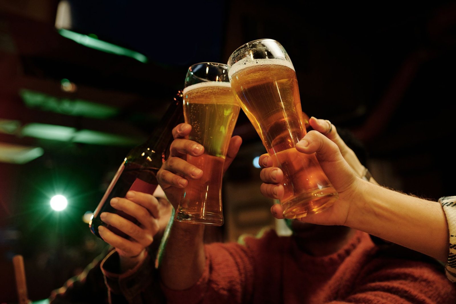 Mãos brindam com copos de cerveja em um bar à noite
