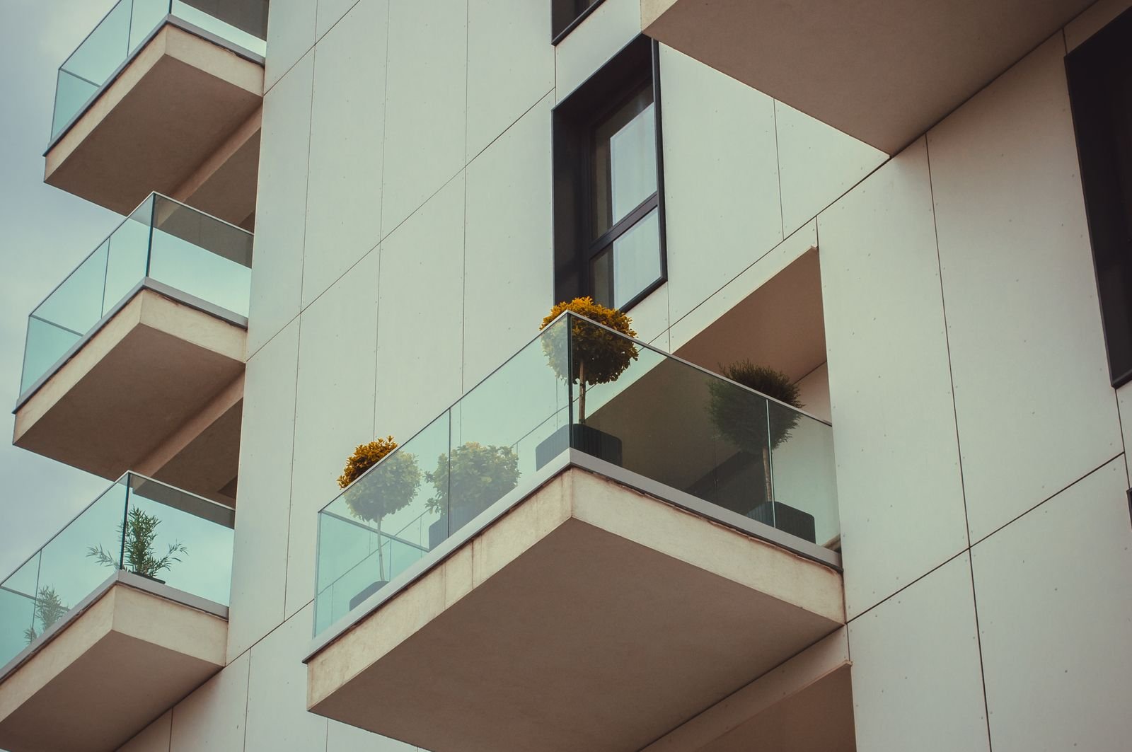 Fachada de prédio residencial moderno com varandas de vidro e vasos de plantas
