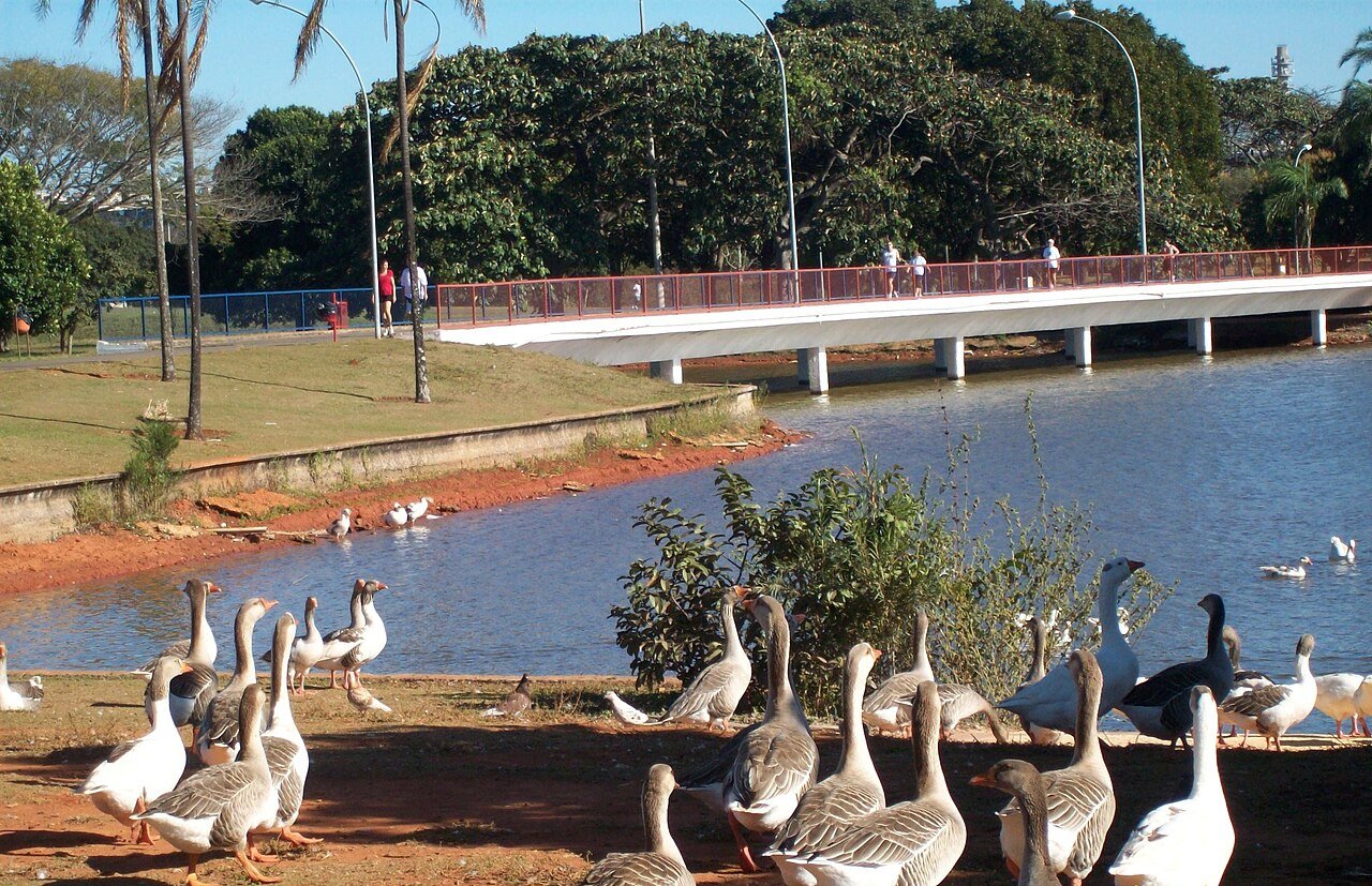 Lago e passarela do Parque da Cidade Sarah Kubitschek, em Brasília, com pessoas caminhando ao fundo