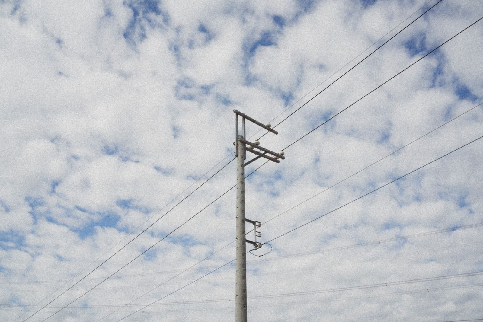 Poste de concreto com cruzetas e fios da rede elétrica recortado contra um céu nublado