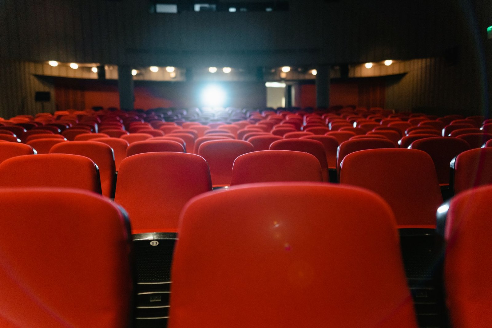 Plateia vazia de cinema com poltronas vermelhas voltadas para a tela iluminada
