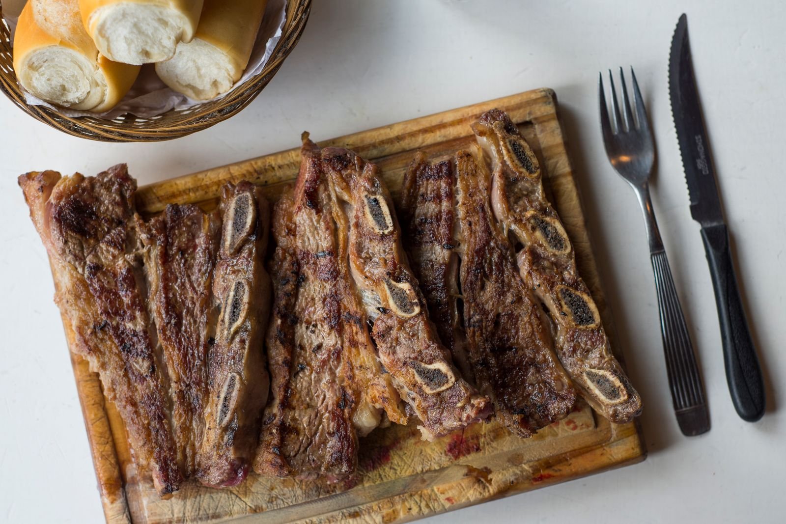 Tábua de costelas de boi grelhadas, com cesto de pão e talheres, em estilo de parrilla argentina