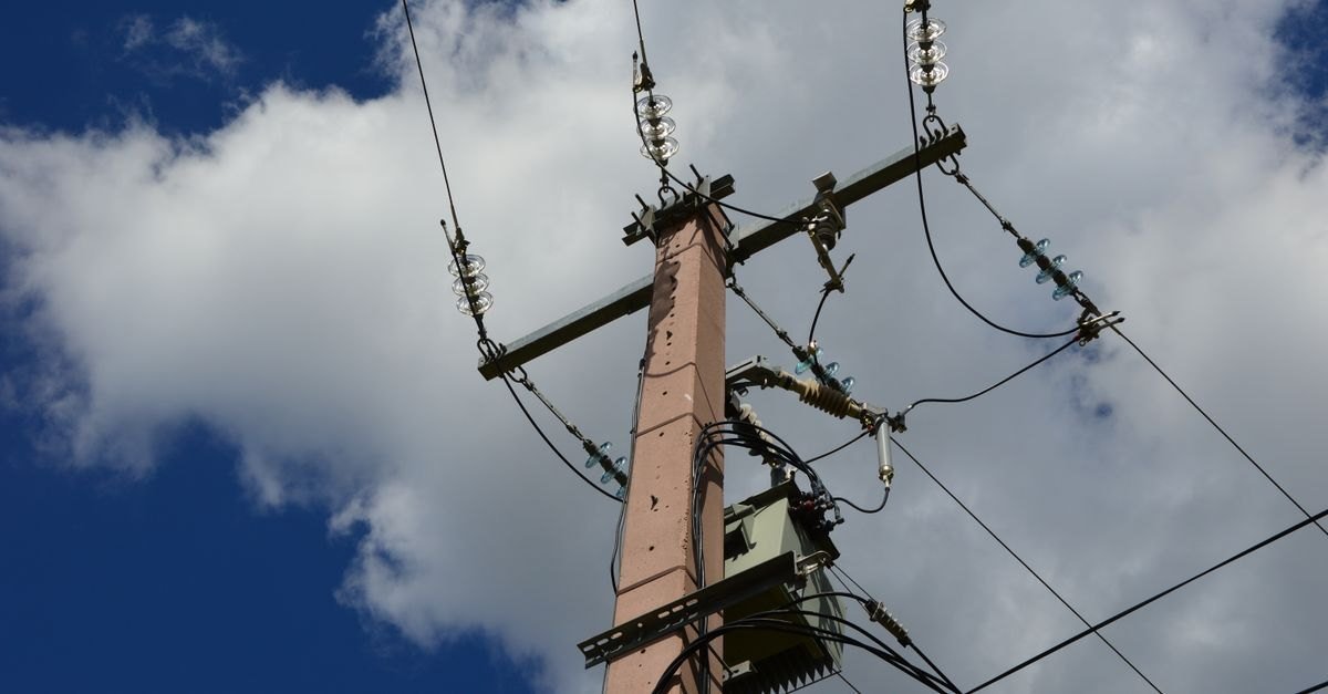 Poste de distribuição de energia elétrica com transformador e isoladores contra o céu azul