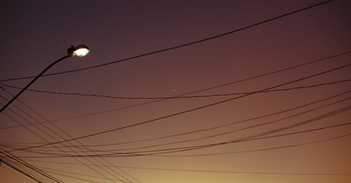 Poste de iluminação pública e fios da rede elétrica recortados contra o céu no fim da tarde