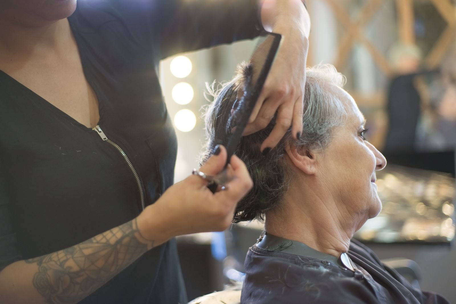 Cabeleireira corta o cabelo de uma cliente idosa em salão