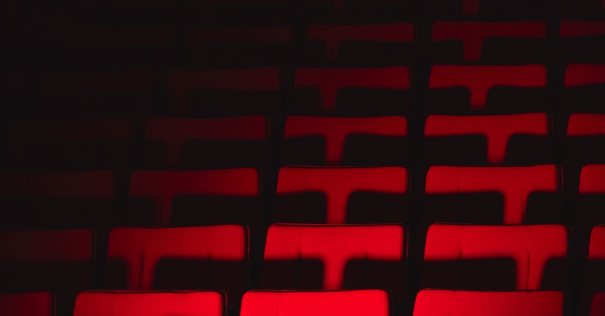 Fileiras de poltronas vermelhas vazias em sala de teatro com iluminacao baixa
