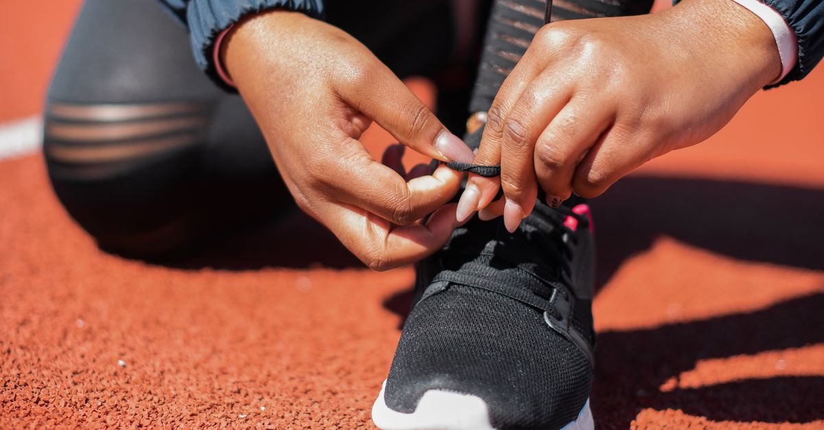 Mãos amarrando o cadarço de um tênis de corrida em pista de atletismo
