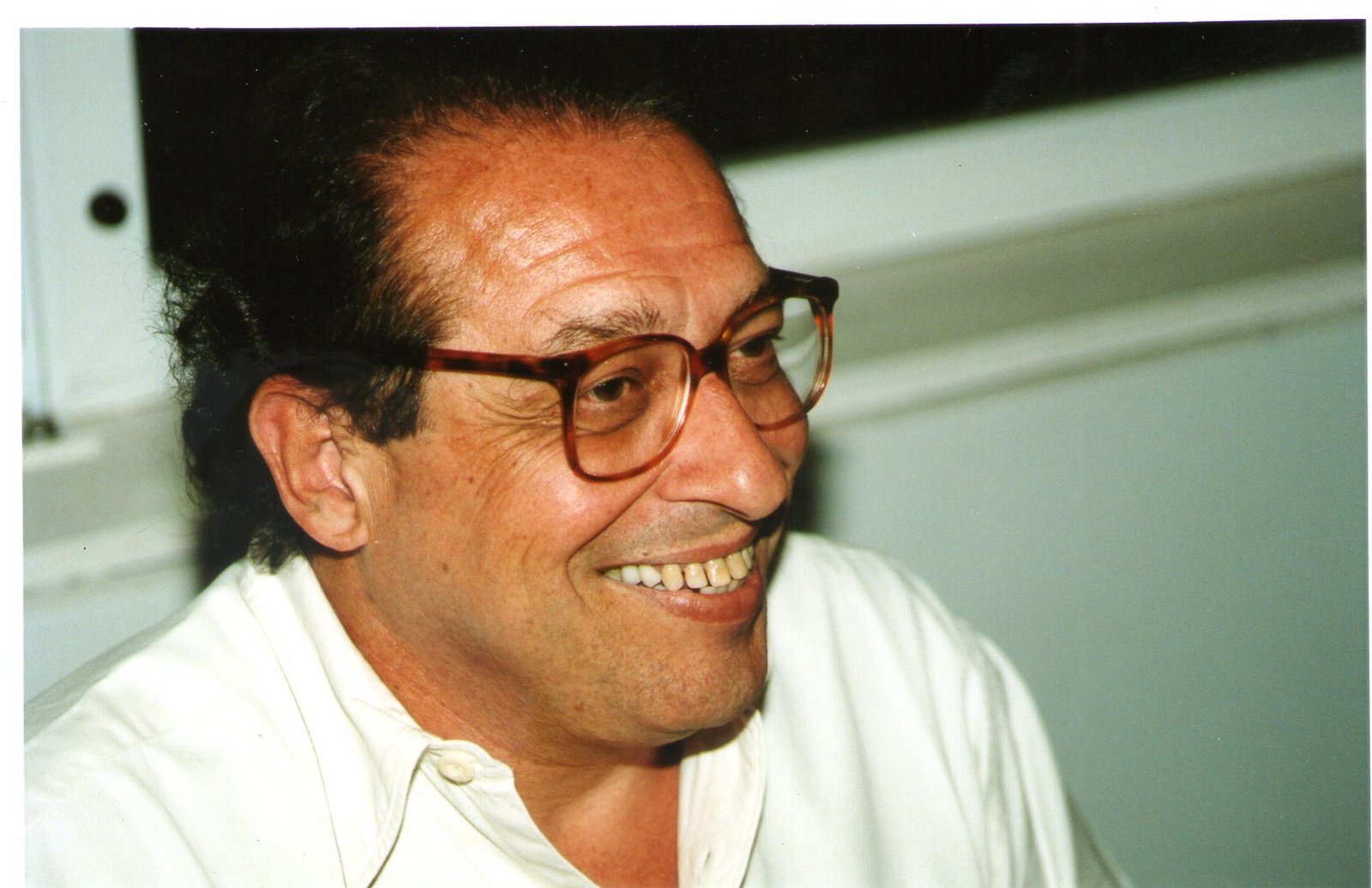 Ruy Castro sorri de perfil, de óculos e camisa clara, em foto de arquivo