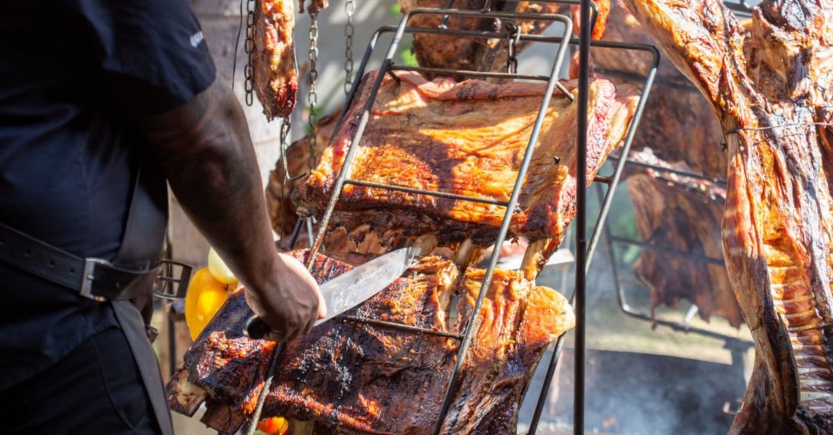 Cozinheiro corta cortes de carne assados em espetos sobre fogo aberto