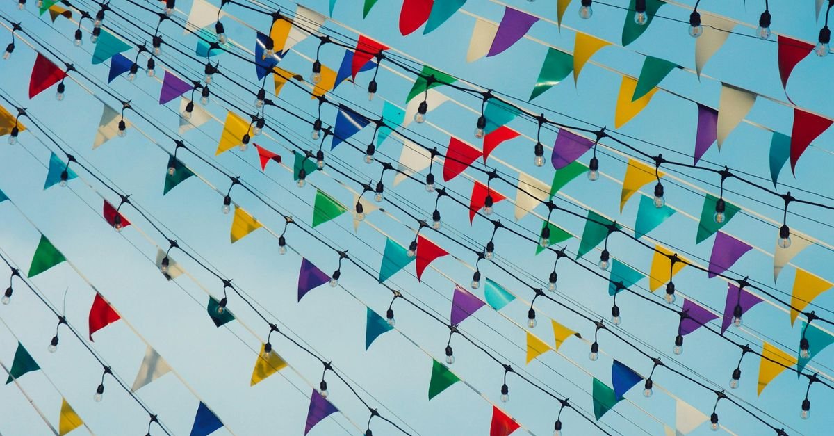 Bandeirinhas coloridas de festa junina penduradas em fios com lâmpadas sob céu azul